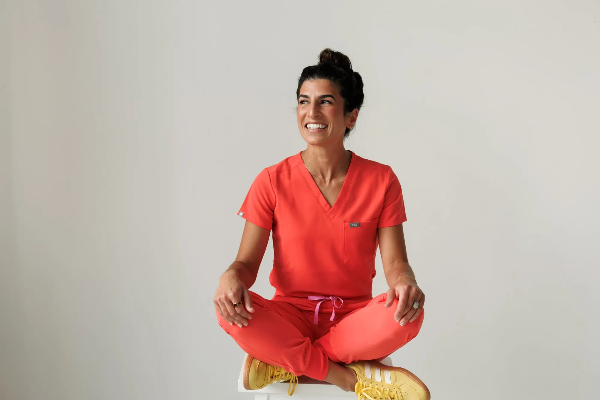 Dr. Miller sitting cross-legged in coral scrubs and yellow sneakers, smiling